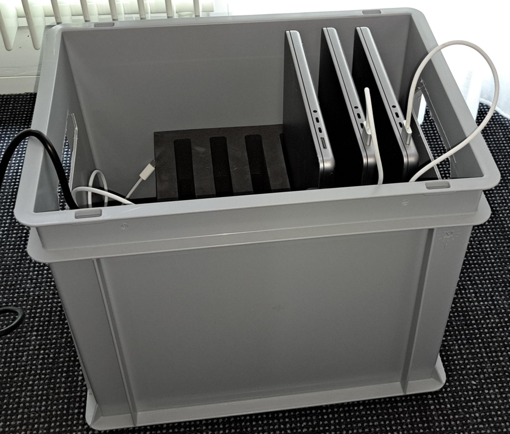 Laptopkiste mit 3 Laptops drin. Die Laptops sind teilweise eingesteckt.